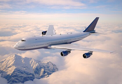 Ein Passagierflugzeug fliegt über einer Wolkendecke, die den Sonnenuntergang reflektiert.