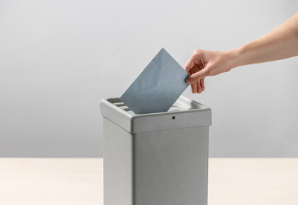 Eine Person steckt einen blauen Umschlag in eine Wahlurne.