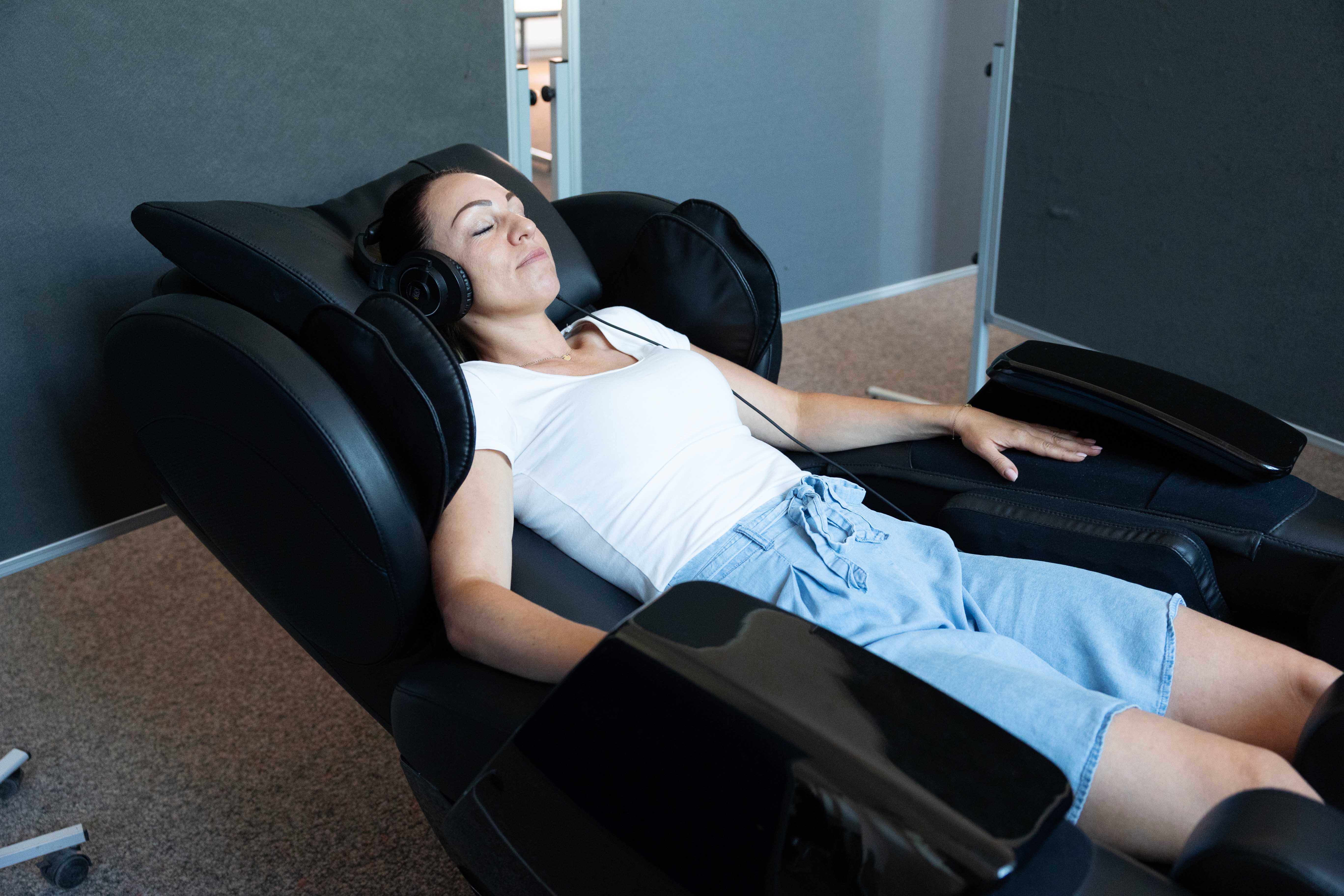 Person mit Kopfhörern liegt entspannt in einem Massagesessel