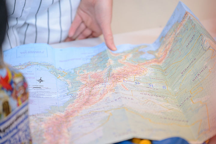 Eine aufgeklappte Weltkarte liegt auf einem Holztisch. Eine Hand hält die Karte fest.