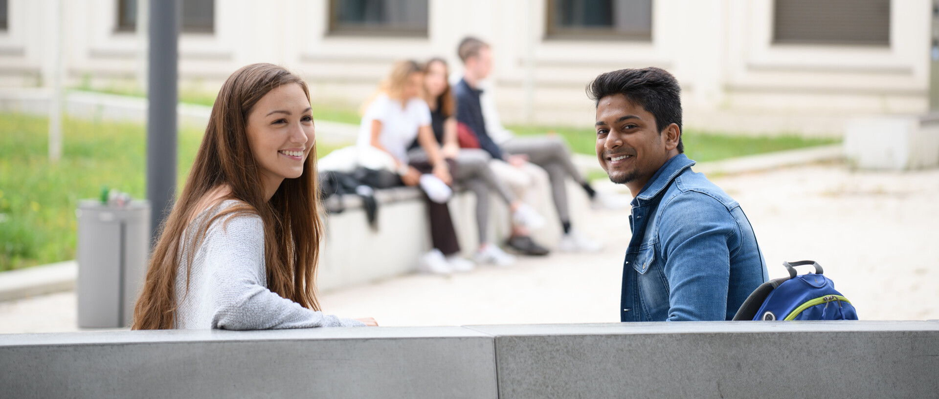 Zwei Studierende sitzen auf einer Bank, wenden sich dem Betrachter zu und lachen. Link: CHE-Masterranking 2023