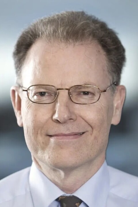 Professor Dr. Colin Atkinson trägt ein helles Hemd, Krawatte und eine Brille und lächelt in die Kamera.