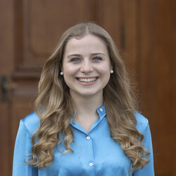 Tonia laughs brightly into the camera. She has long, dark blonde hair and is wearing a blue blouse.