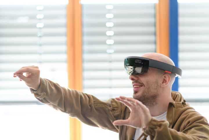 Ein Mensch trägt eine Virtual-Reality-Brille und hebt seine Hände hoch.