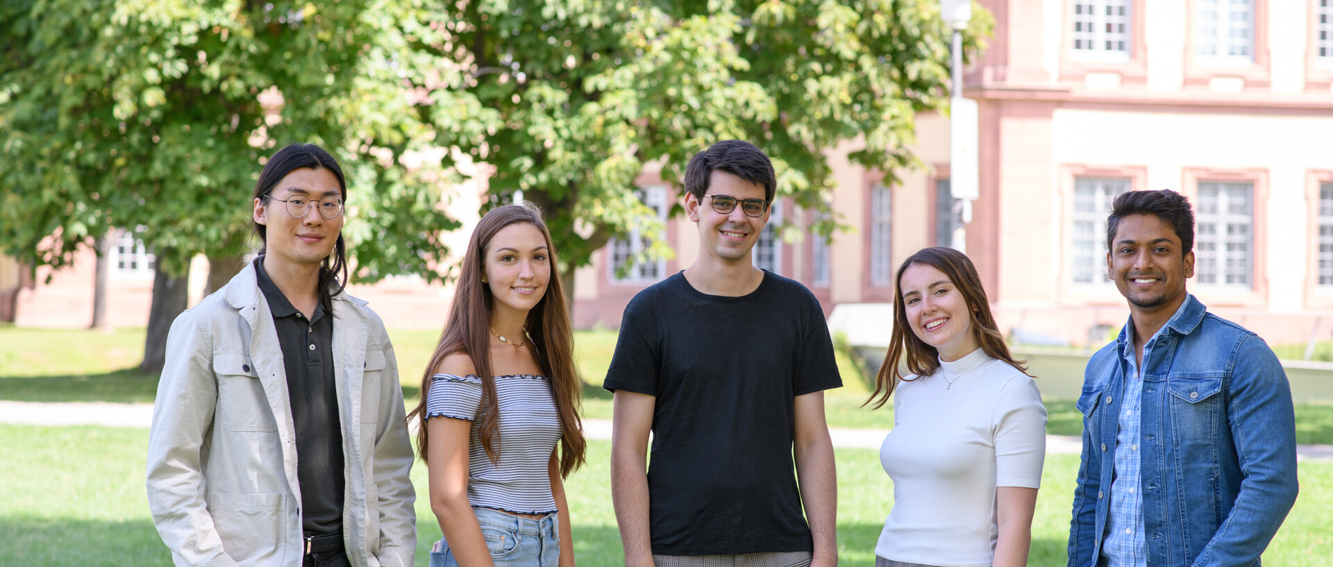 Fünf junge, internationale Studentinnen und Studenten auf einer Wiese am Schloss