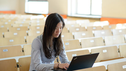 Frau mit Laptop im leeren Vorlesungssaal
