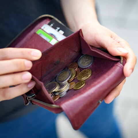 Eine Person zeigt ihre geöffnete Geldbörse. In dieser sind Münzen und verschiedene Karten.
