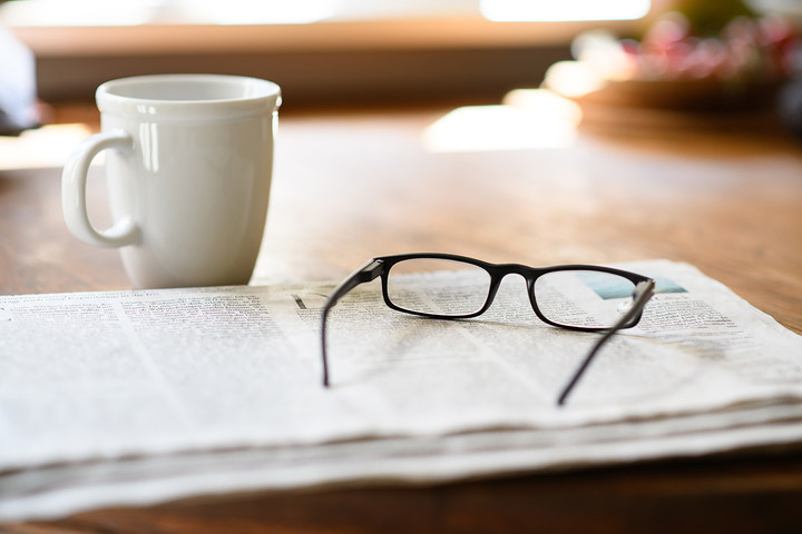 Auf einem Tisch liegt eine Zeitung, darauf eine Brille und daneben eine Kaffee-Tasse. Link: Leistungen