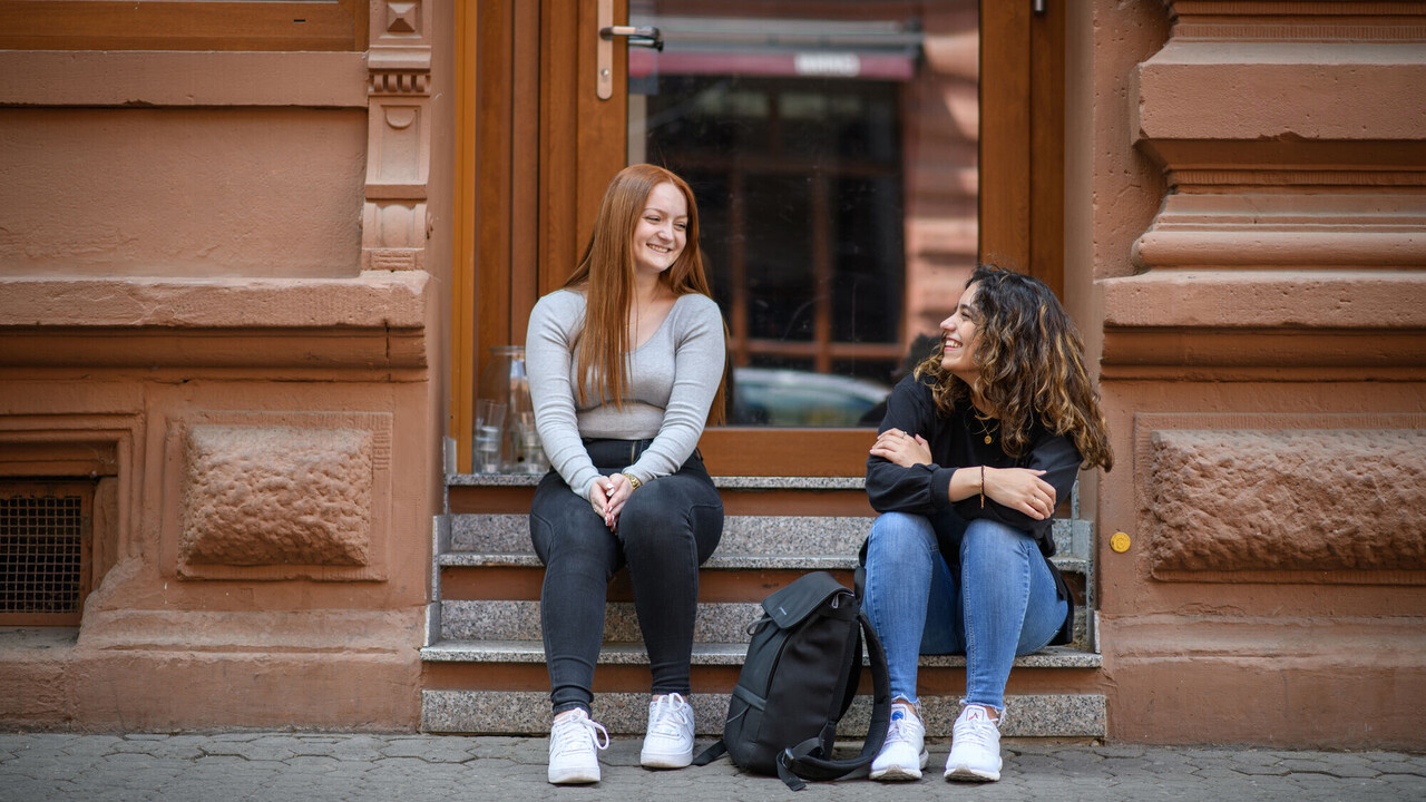 Zwei Studentinnen auf der Steintreppe eines Wohnhauses