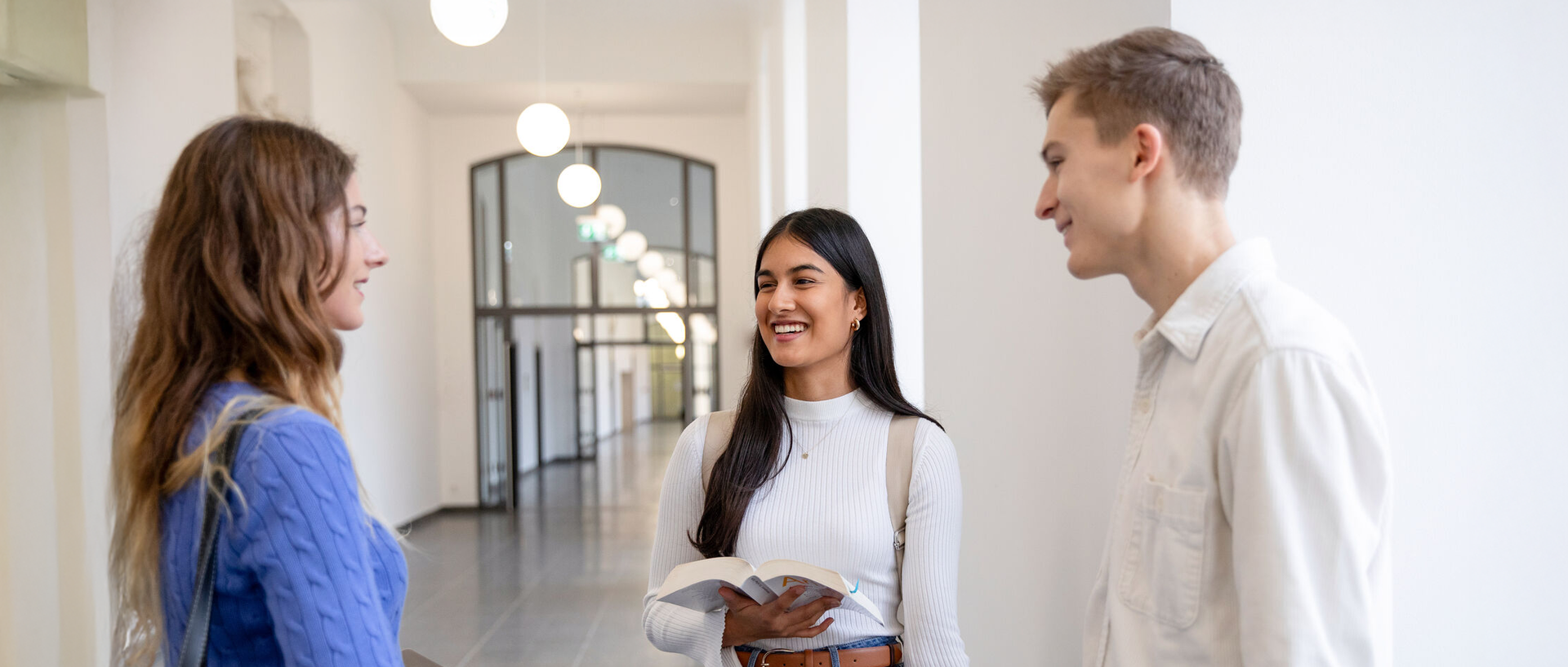 CHE Masterranking 2025 Drei Studierende stehen auf einem Flur im Mannheimer Schloss und unterhalten sich.