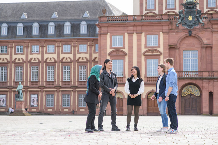 Fünf Studierende stehen auf dem Ehrenhof des Schlosses und reden miteinander.