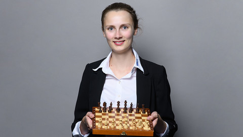 Eine lächelnde Person trägt eine weiße Bluse sowie einen schwarzen Blazer und hält ein Schachbrett in den Händen. Die Person heißt Josefine Heinemann.