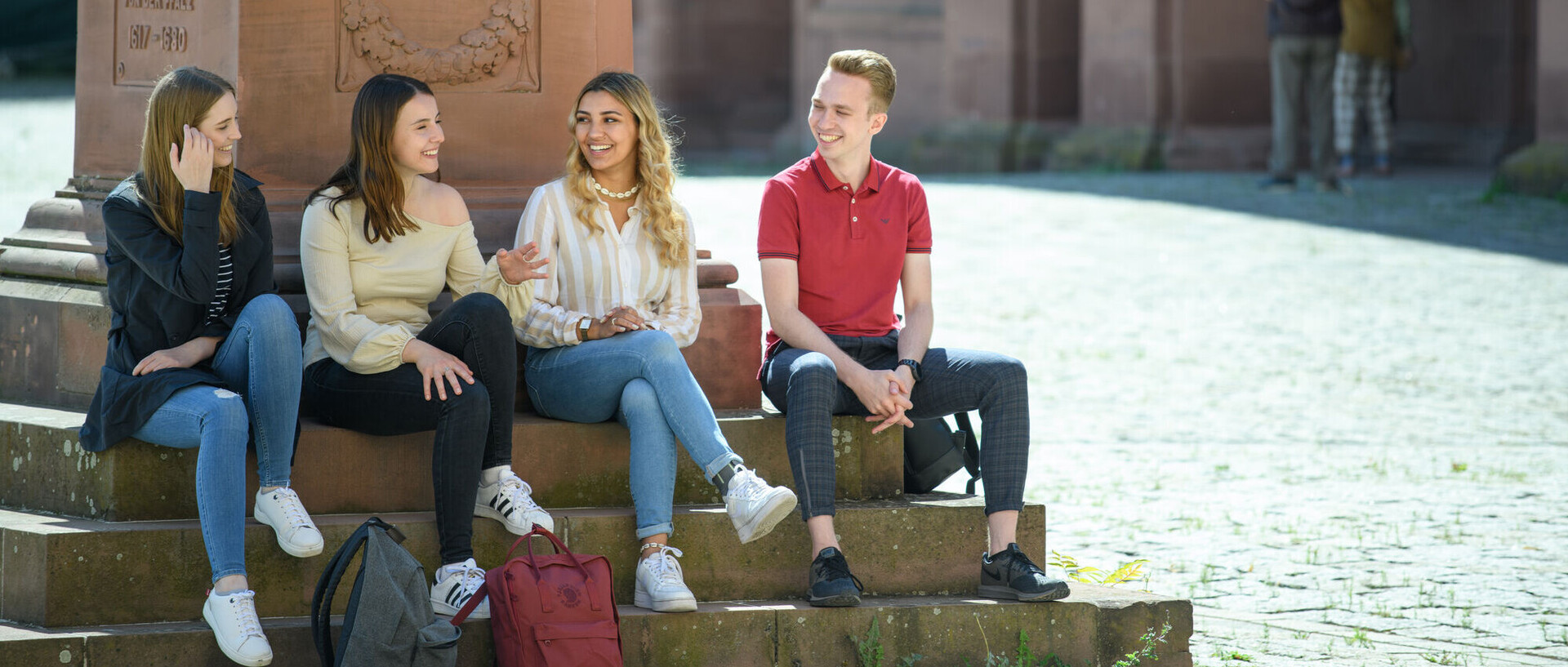 Shanghai Subject Ranking 2025 Vier Studierende sitzen auf den Stufen einer Statue auf dem Ehrenhof. Sie lachen.