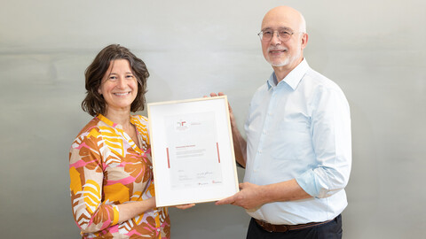 Kanzlerin Katrin Schoppa-Bauer und Rektor Thomas Puhl halten ein Zertifikat in den Händen und lächeln in die Kamera.