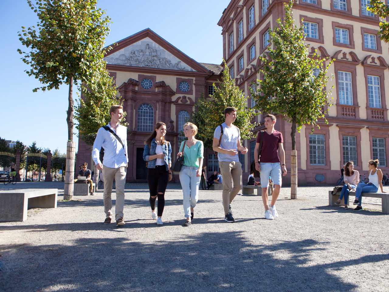 Studierende laufen bei Sonnenschein über den Ehrenhof des Schlosses.