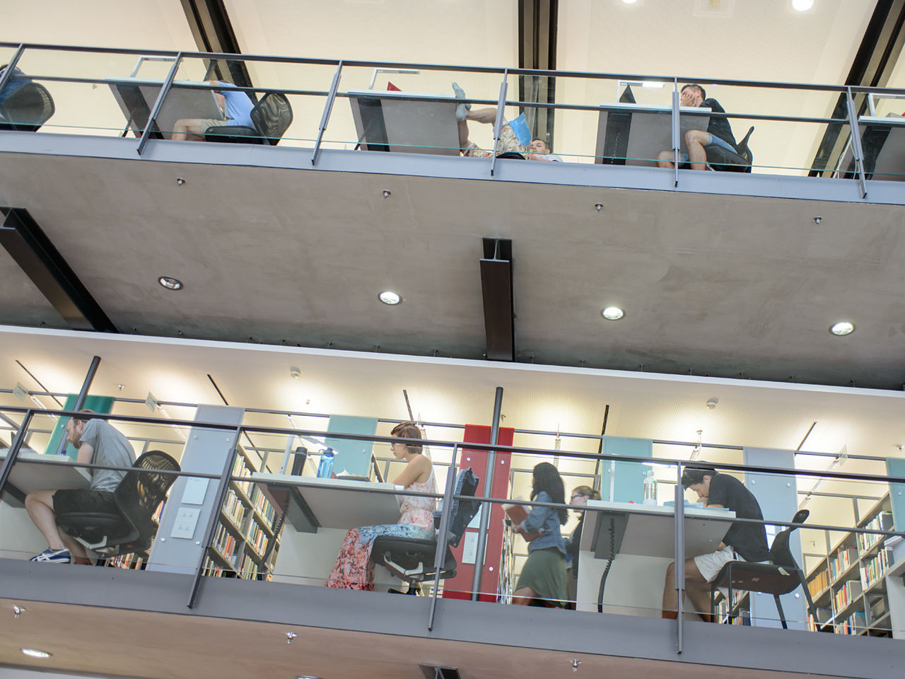 Studierende sitzen auf verschiedenen Etagen der Bibliothek an Arbeitsplätzen.