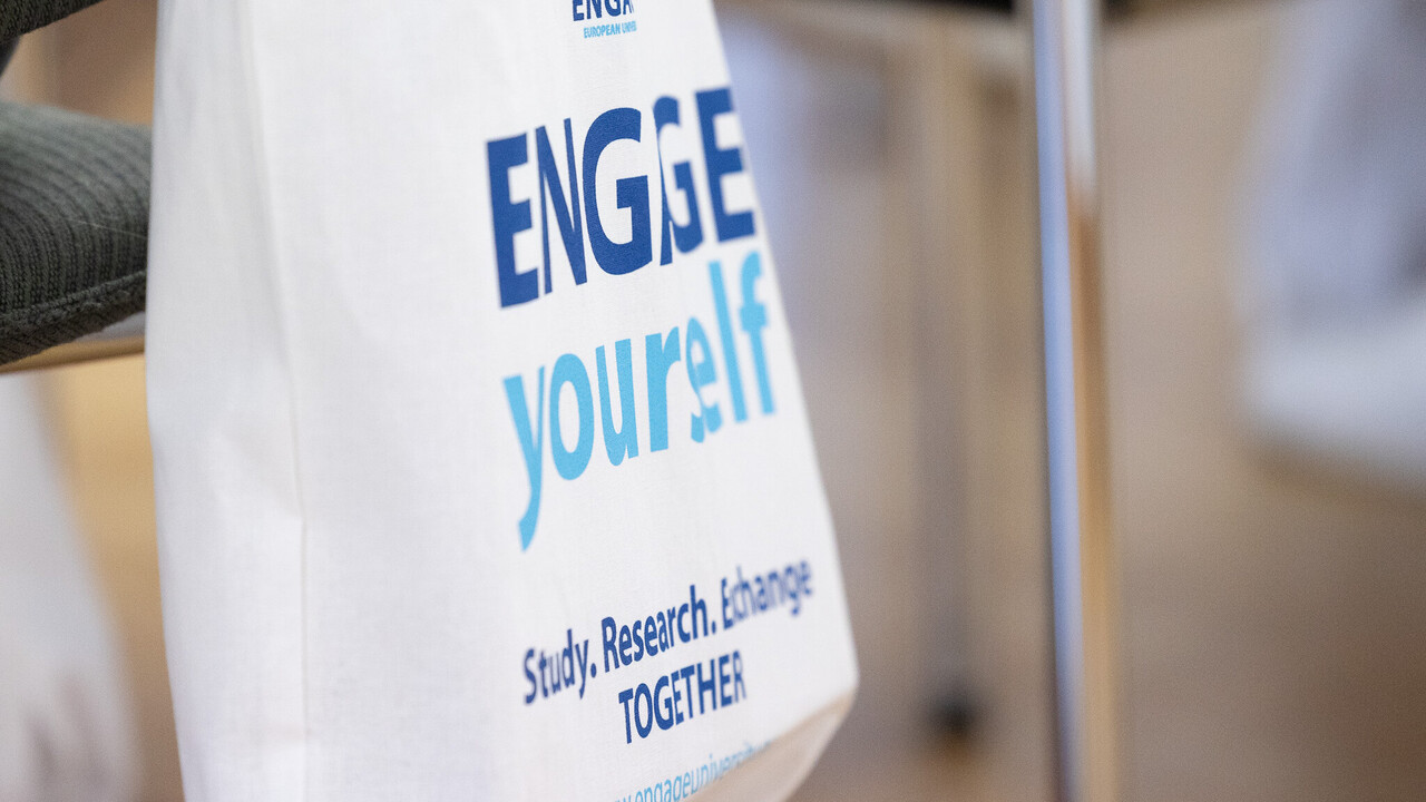 Eine Stofftascher hängt an einem Stuhl. Sie trägt die folgende Aufschrift: "Engage yourself. Study, research, exchange together."
