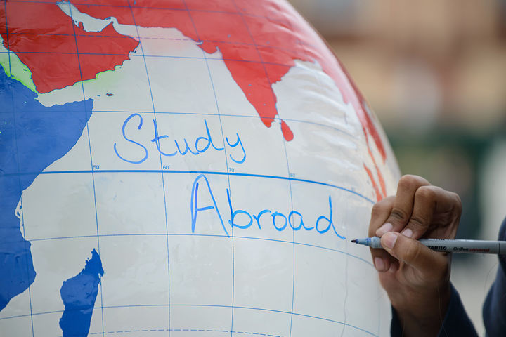 Eine Hand schreibt "Study Abroad" auf einen aufgeblasenen Globus