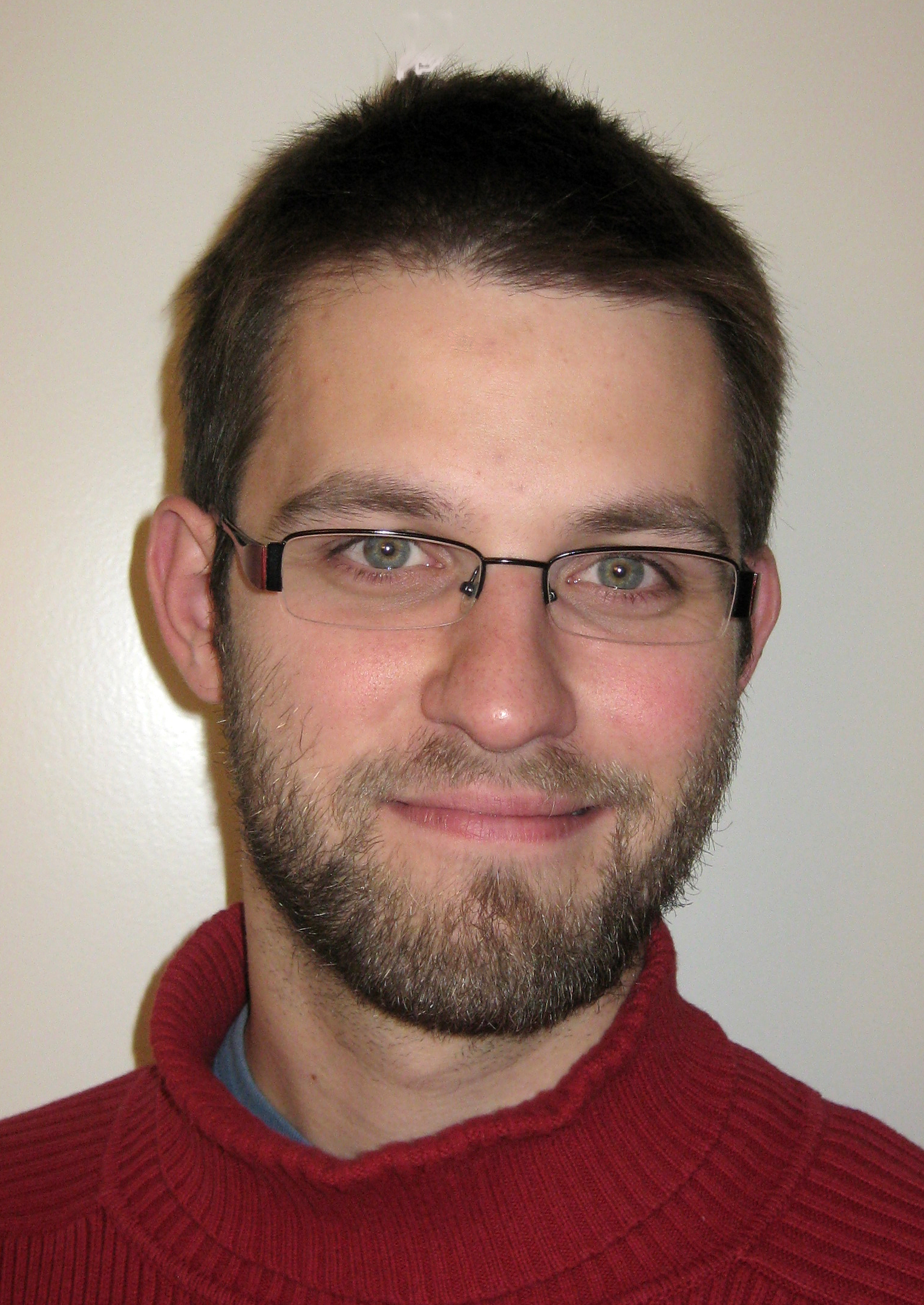 Portrait von Stefan Janke. Er trägt einen roten Rollkragenpullover und lächelt.