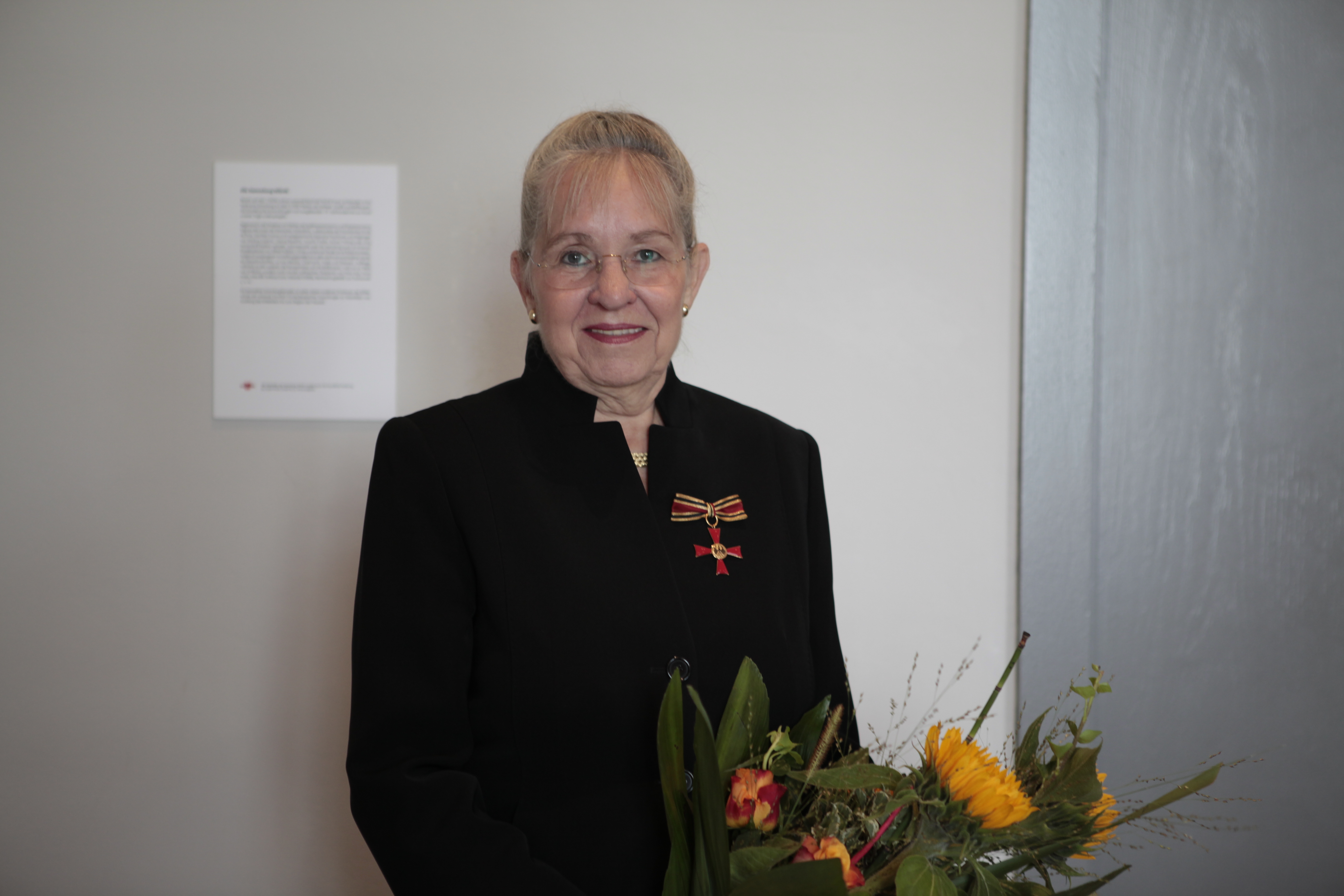 Dorothee Dickenberger steht vor einer Wand und hält einen Strauß Blumen in der Hand.