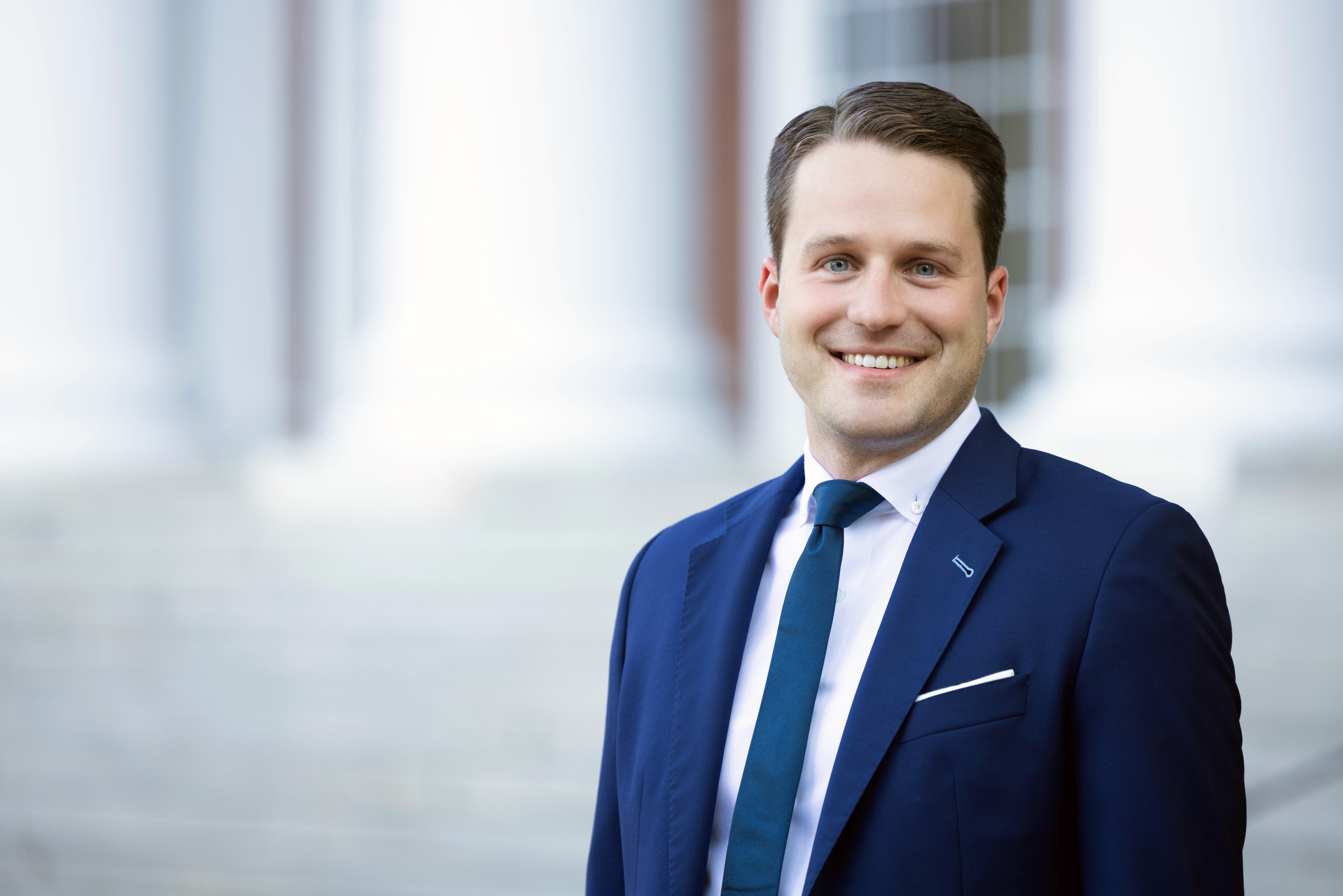 Gunther Glenk trägt einen blauen Anzug mit einer blauen Krawatte und lächelt.