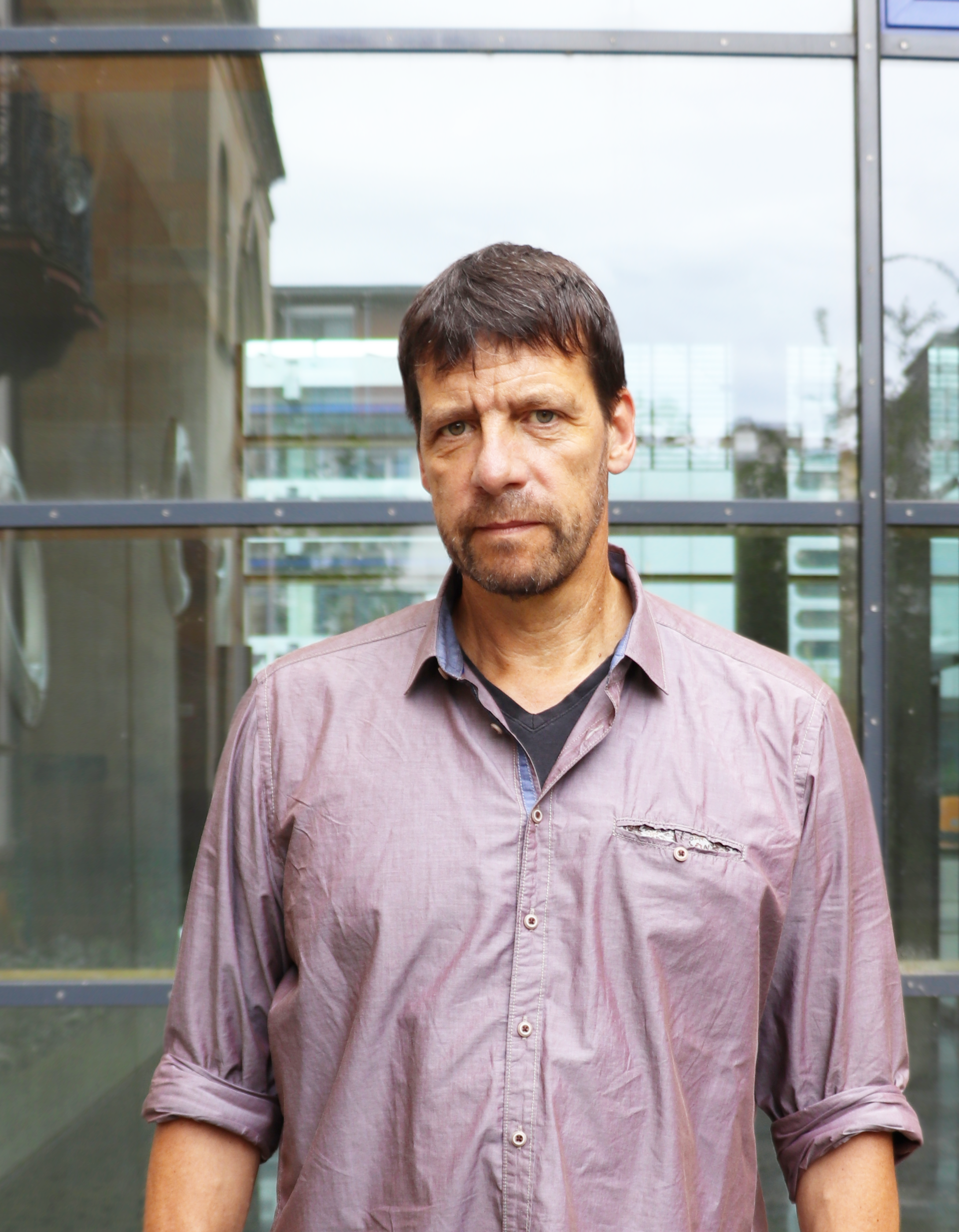 Porträt von Professor Krause, der vor einer Glaswand steht, ein lilafarbenes Hemd trägt und in die Kamera schaut.