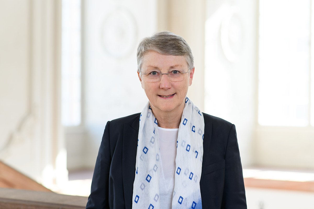 Portrait von Barbara Windscheid. Sie trägt einen dunkelblauen Blazer sowie einen weißen Schal mit blauen Rechtecken. 