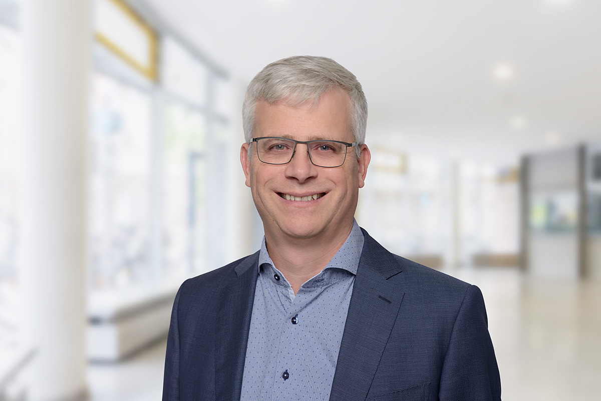 Portrait von Eckhard Janeba. Er trägt ein blaues Hemd sowie einen blauen Anzug und lächelt.