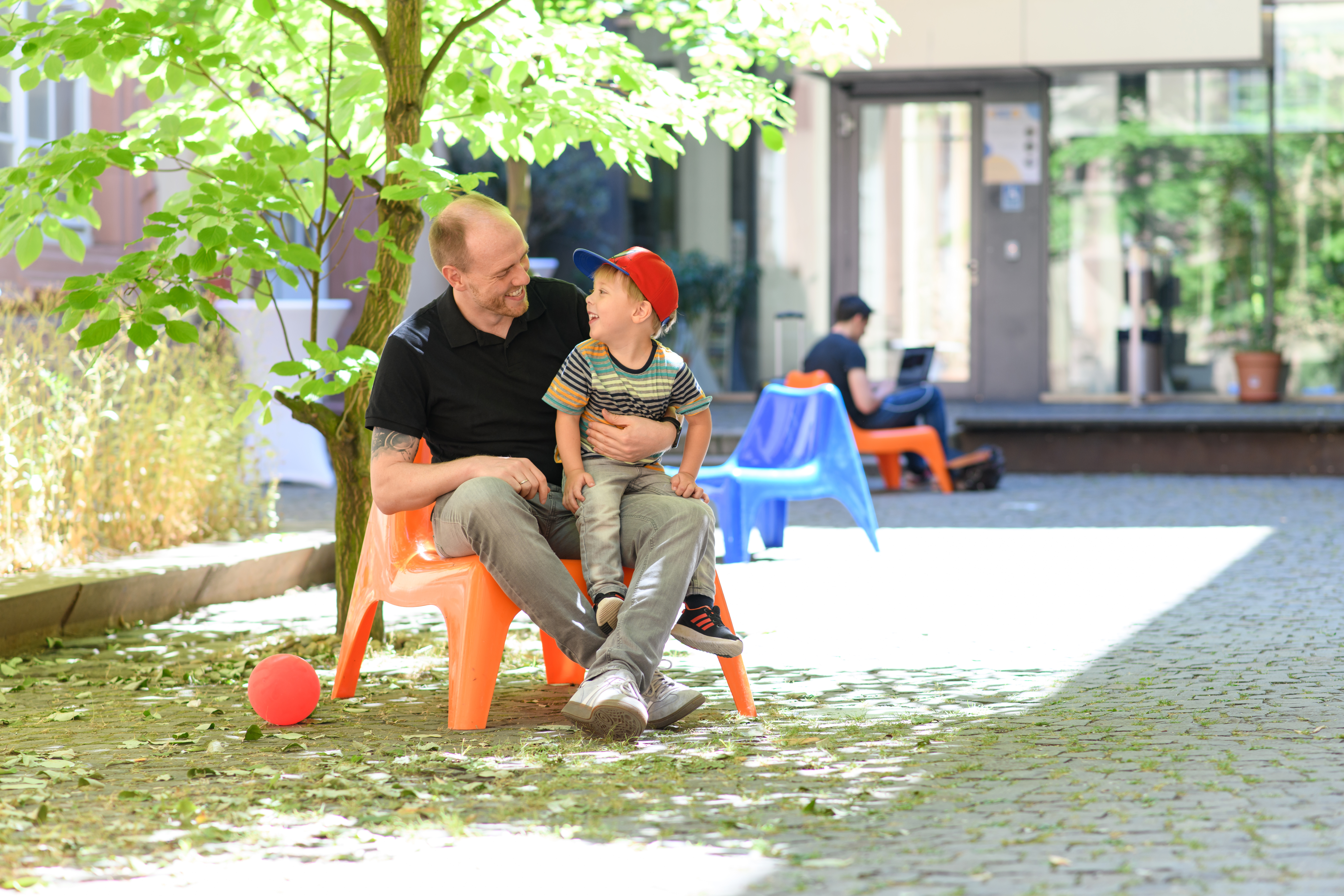 Father and son are sitting on the campus of the University of Mannheim and smiling at each other.