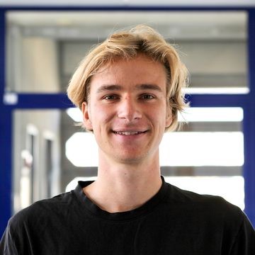 Oliver Rittmann steht vor einer Glastür. Er trägt einen dunklen Pullover und hat hellblonde Haare.