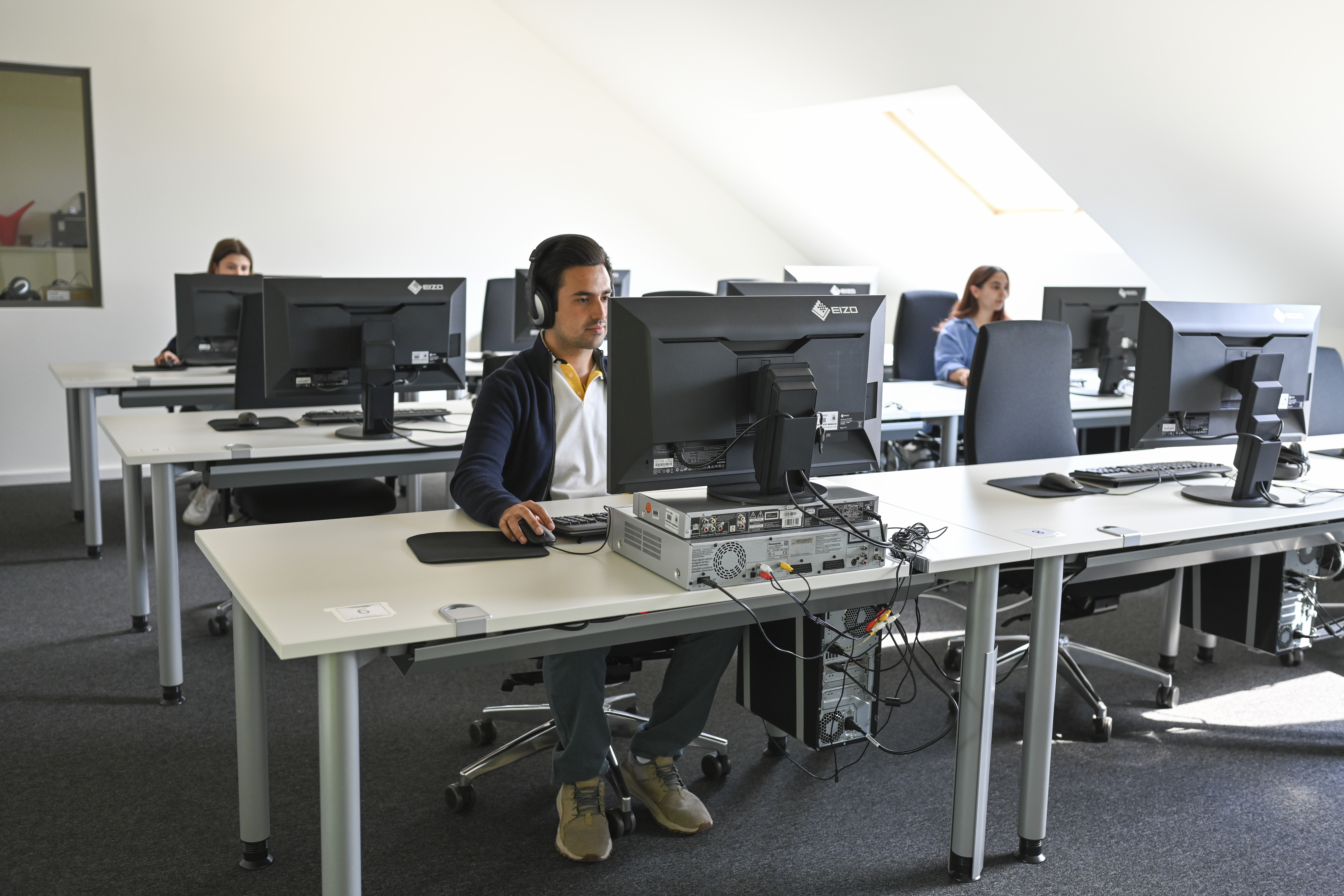 Drei Studierende arbeiten mit Kopfhörern an den Medienschnittplätzen.