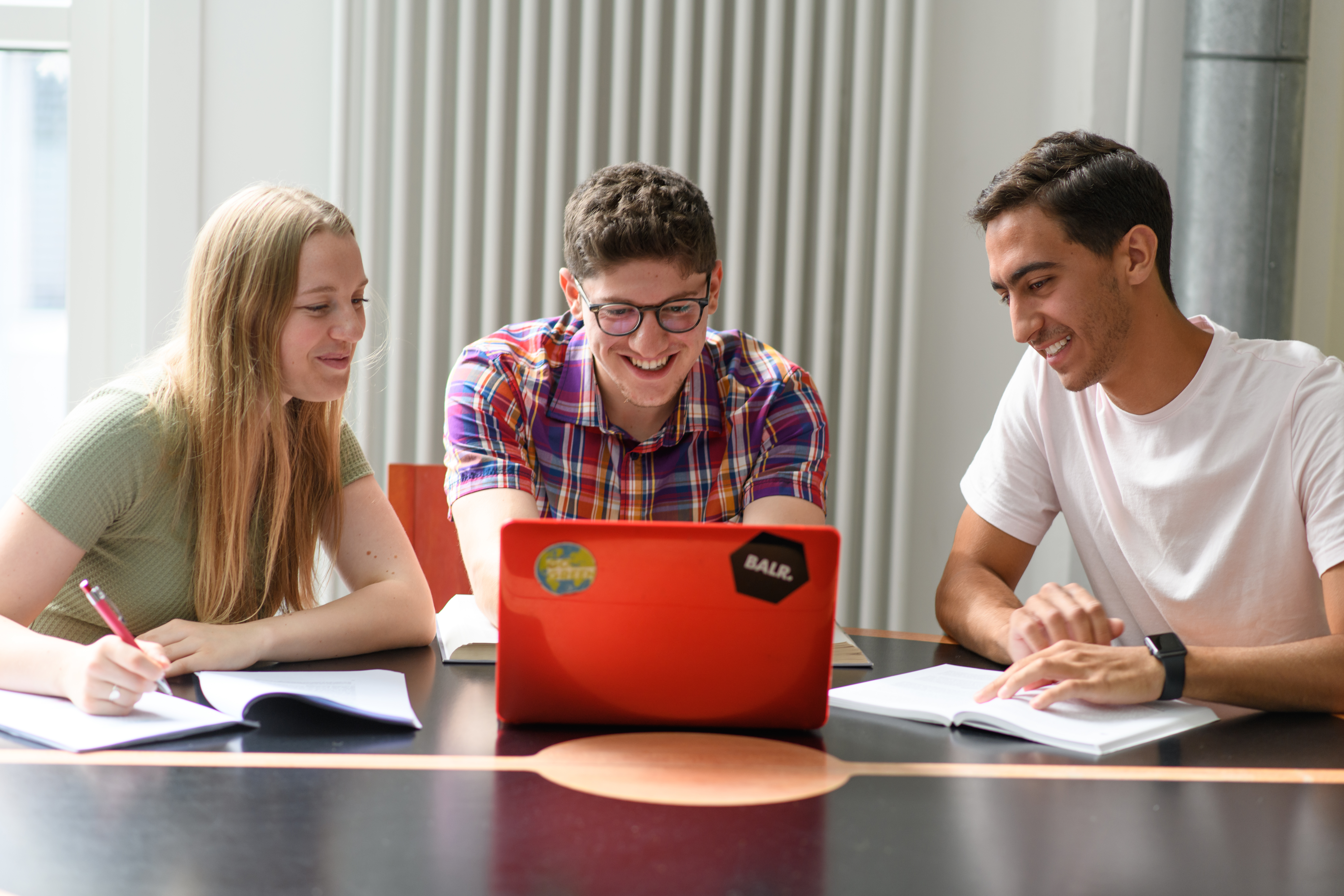 Drei Studierende sitzen an einem Tisch an einem Laptop