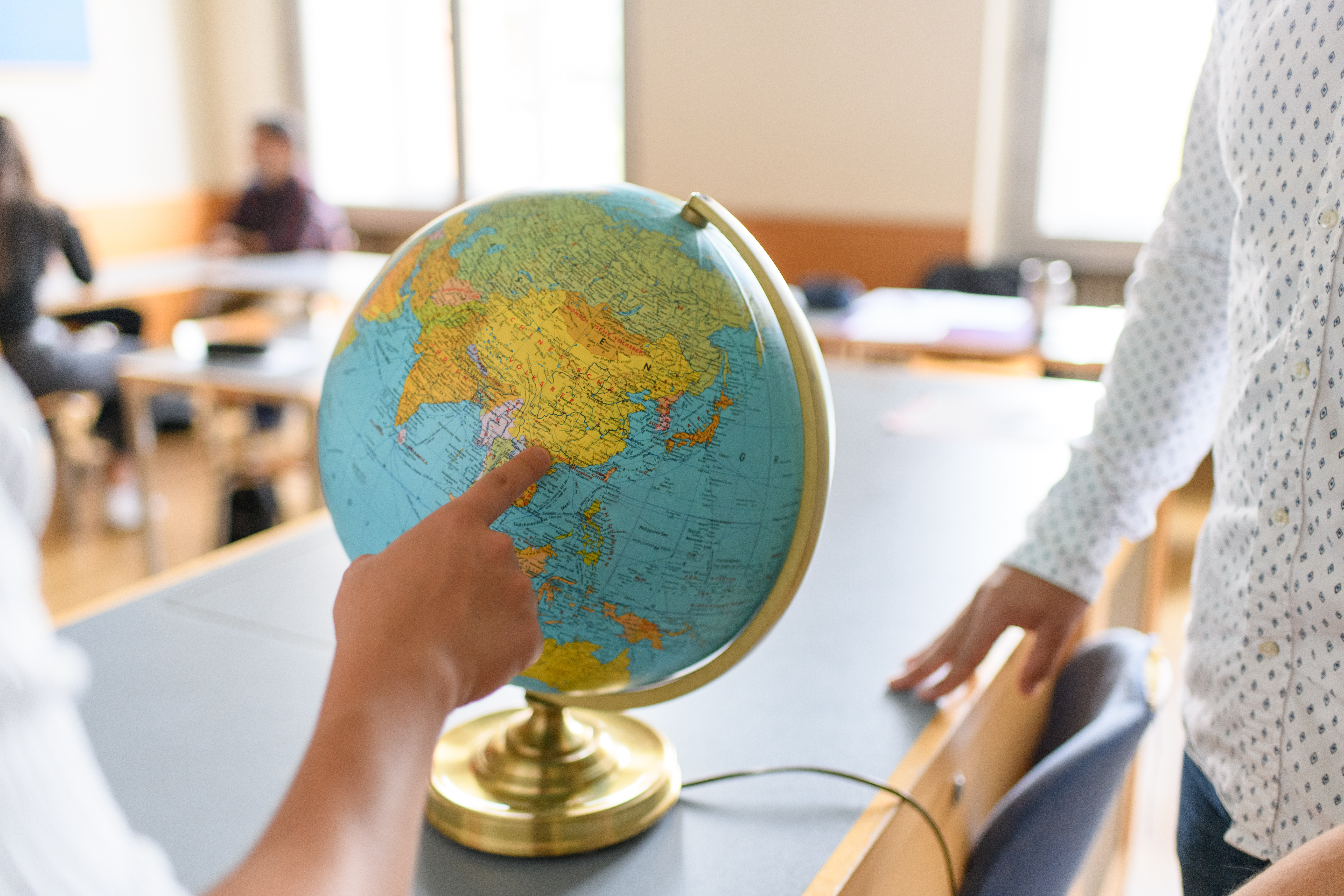 Eine Person zeigt auf einen Globus. Dieser steht auf einem Schreibtisch in einem Seminarraum des Mannheimer Schlosses.