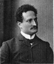 Ludwig Frank in dunklem Anzug und mit hellem Hemd. Er trägt kurzes dunkles Haar und einen Schnurrbart. 