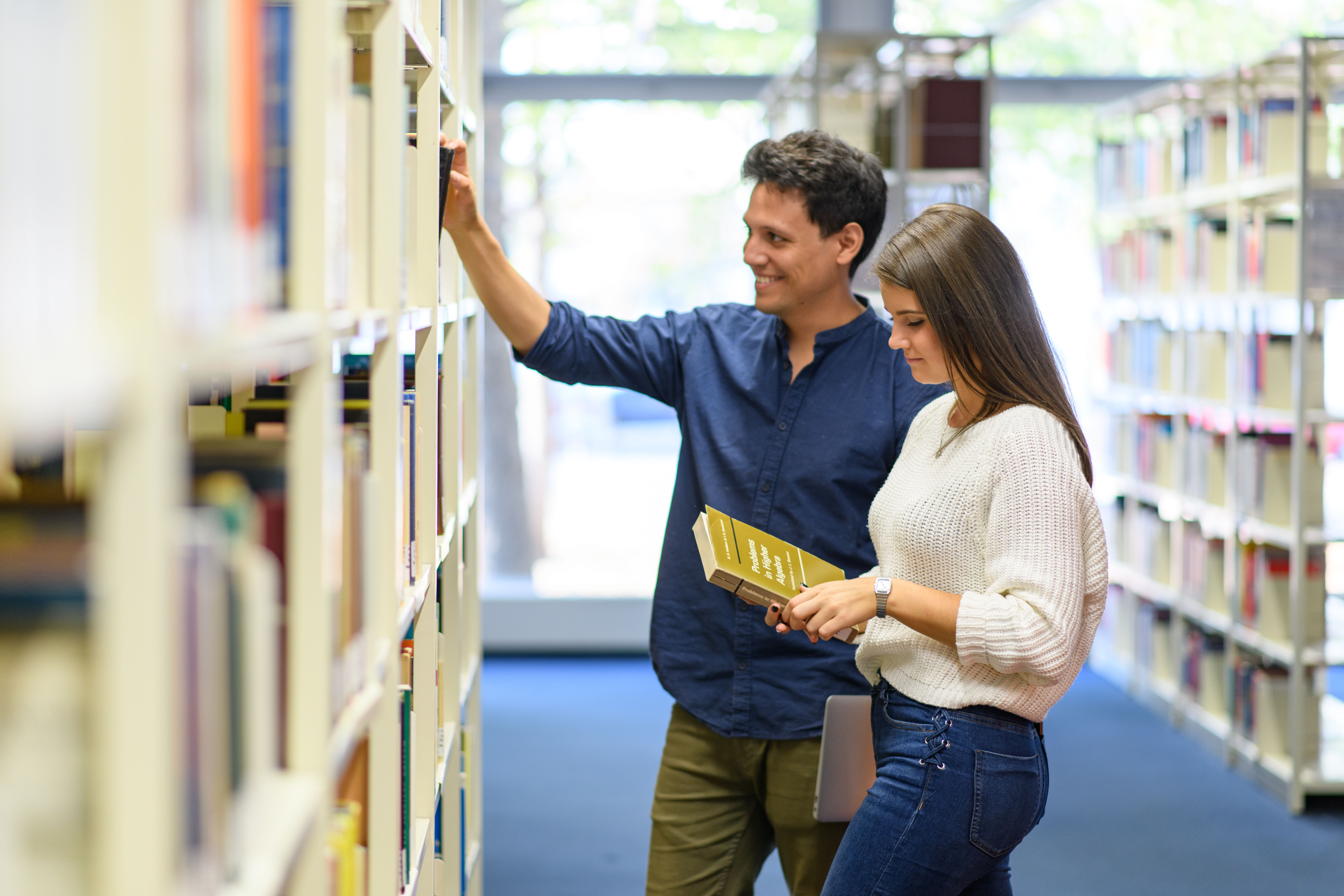 Student und Studentin nehmen Bücher aus dem Bücherregal