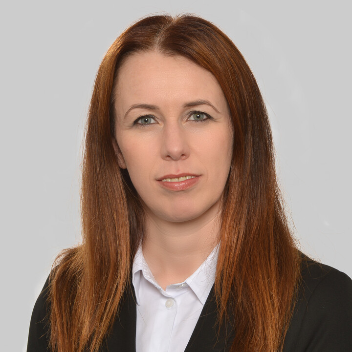 Eine Frau mit schwazem Blazer vor einem grauen Hintergrund
