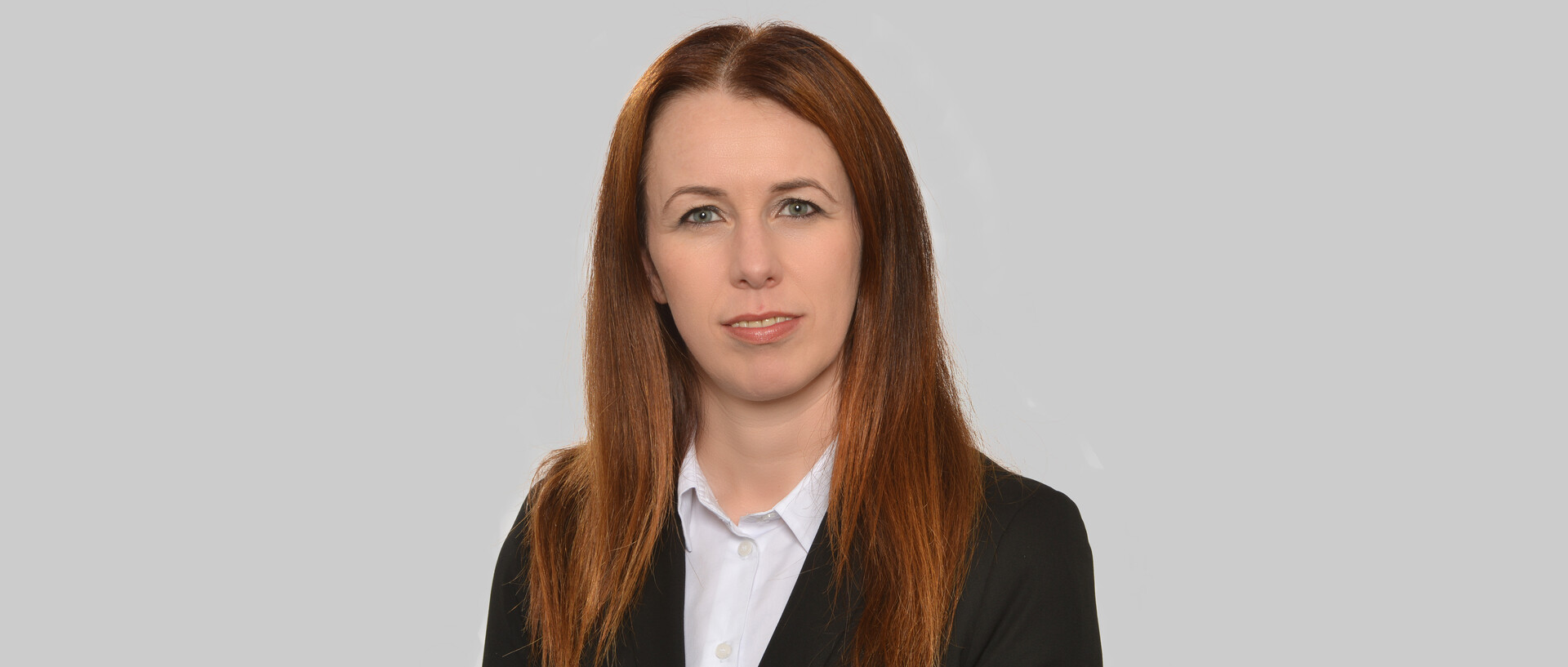Eine Frau mit schwazem Blazer vor einem grauen Hintergrund