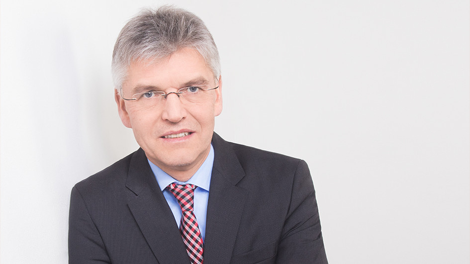 Portrait von Christoph Spengel. Er trägt ein schwarzes Jackett und lehnt an eine weiße Wand.