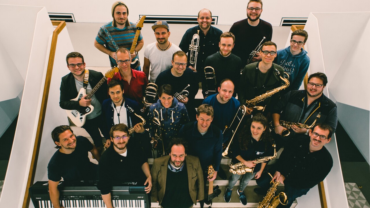 Mitglieder eines Orchesters stehen mit ihren Instrumenten auf einer Treppe.