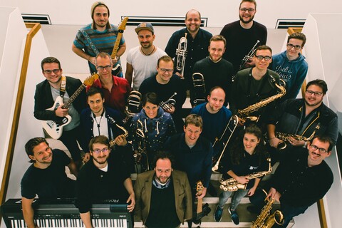Mitglieder eines Orchesters stehen mit ihren Instrumenten auf einer Treppe.