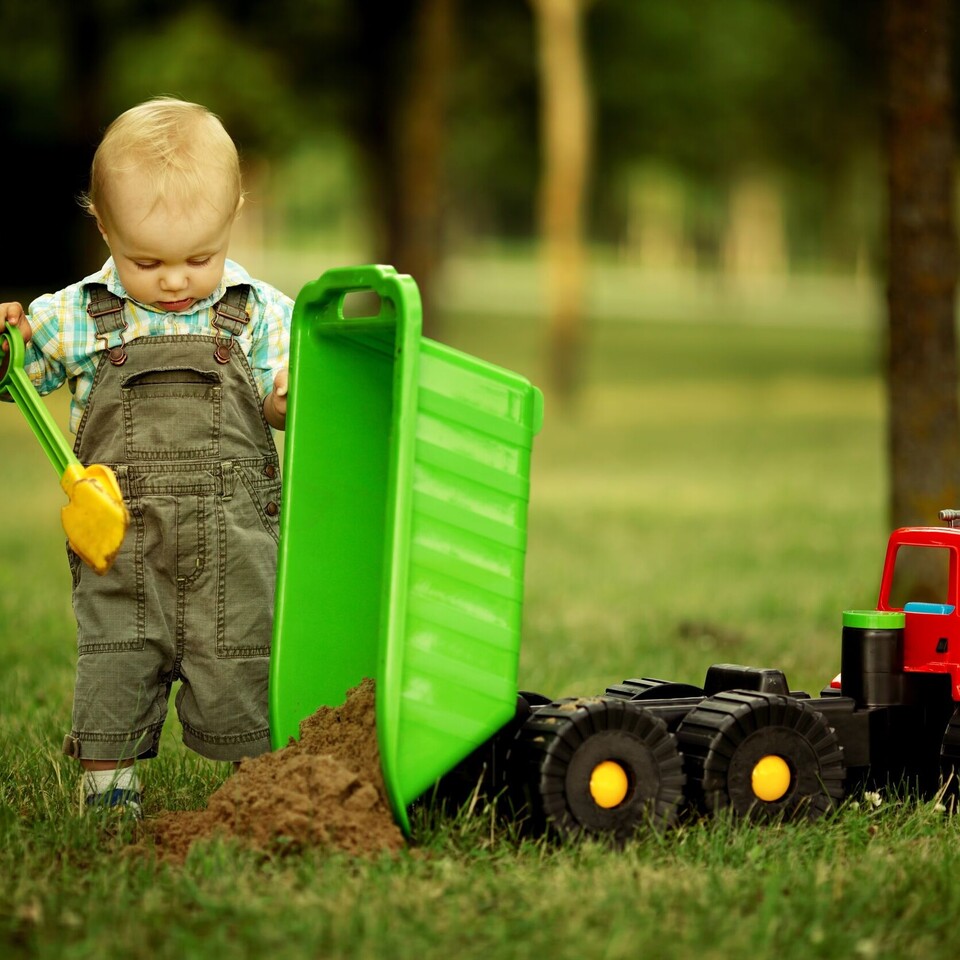Ein Kind kippt Sand aus einem Spielzeug-Laster.