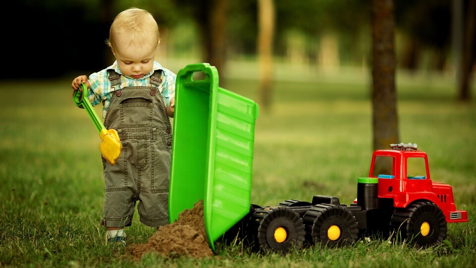 Ein Kind kippt Sand aus einem Spielzeug-Laster.