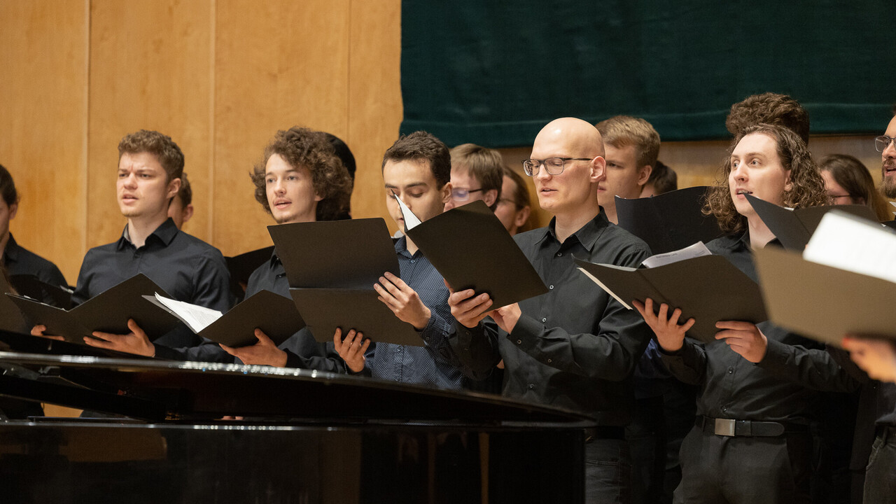 Männliche Chormitglieder halten ihre Noten in der Hand und singen.