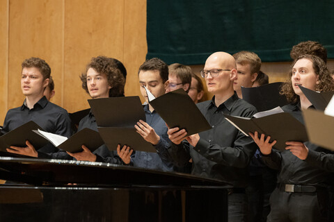 Männliche Chormitglieder halten ihre Noten in der Hand und singen.