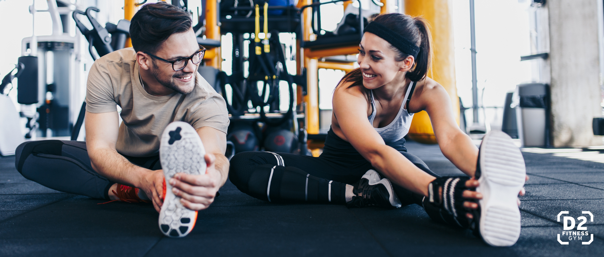 Mann und Frau machen zusammen Dehnübungen af dem Boden im Fitnessstudio