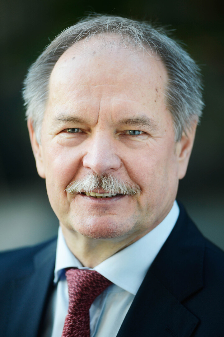 Dr. Peter Merten Portrait von Peter Merten. Er trägt ein weißes Hemd, eine rote Krawatte sowie einen schwarzen Blazer und lächelt.