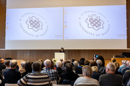 Foto von einer Veranstaltung des Gasthörendenstudiums in der Aula. Am Pult steht eine Referentin, vor ihr sitzen die Zuhörenden.