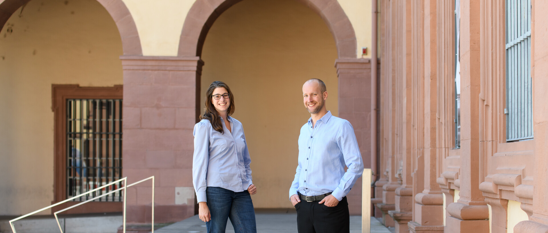 Ein Mann und eine Frau stehen auf dem Gelände der Universität Mannheim und blicken zur Kamera.
