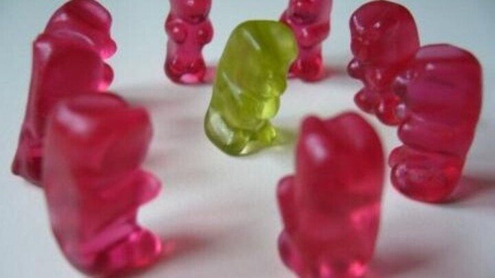 Acht rote Gummibärchen sind in einem Kreis angeordnet. In der Mitte des Kreises steht ein grünes Gummibärchen.
