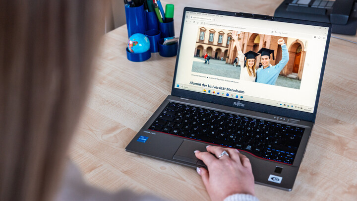 An einem Laptop ist die Alumni-Webseite der Universität geöffnet. Eine Hand liegt auf dem Touchpad.